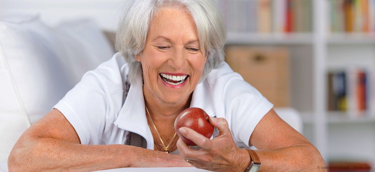 ältere dame schaut einen apfel an und lacht mit schönen zähnen